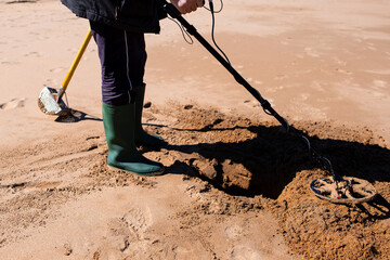 Person using metal detector on sandy beach for buried treasures