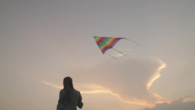 Free girl launches a kite into the sunset sky, have fun on the journey, play in the fun outdoors of nature, dream to fly, women's weekend with rainbow color play in nature, catch the wind high above.