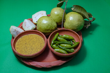 Vibrant arrangement of fresh green guavas (whole and sliced), green chilies, and Kasundi (a popular Bengali spicy mustard sauce) presented in earthen bowls