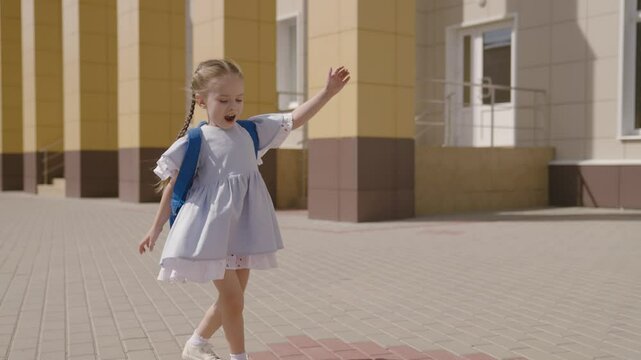 Little child with school backpack having fun spin in school yard, happy dreamy kid, first grader loves to play dizzying games, fun game for childhood, education and development preschool age outdoors.