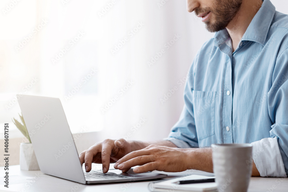 Poster handsome male freelancer working on laptop at desk in home office, answering emails, typing on compu