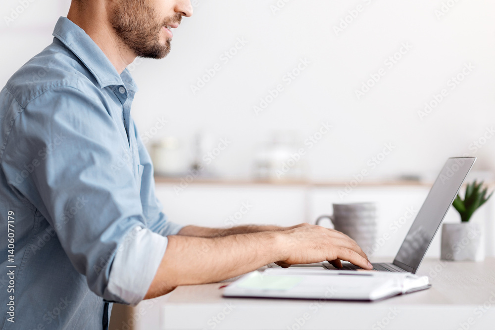 Poster handsome millennial businessman sitting at workplace in white office, working on laptop, typing on c