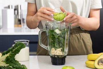 Woman making green smoothie, adding green kiwi to blender. Detox, vegan food 