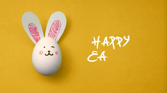 Horizontal 4K video. Stop motion, frame by frame animation. Egg hunt. Chicken egg with cute bunny face, paper rabbit ears and white hand drawn text Happy Easter on light yellow table. Greeting card	