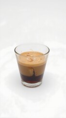 A captivating close up of a finely layered espresso shot in a clear glass elegantly displayed on a crisp white background with dramatic lighting