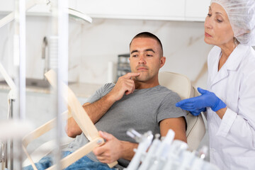 Obraz premium Man looks in the mirror and consults a professional female plastic surgeon