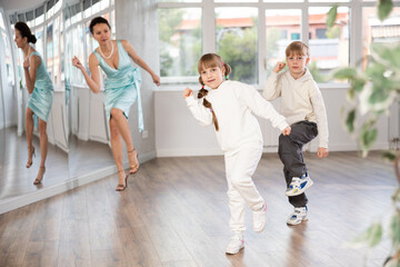 Boy and girl kids repeat movement while taking boogie woogie dancing lessons. Female teacher conducts class for students during dance workout and watches performing movements