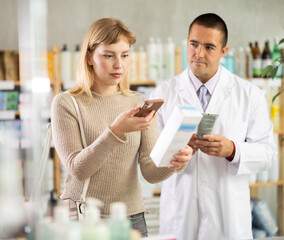 Attentive young girl scanning barcode of cream and apothecary giving offer in drugstore
