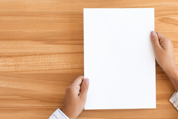Fototapeta premium Overhead view of woman holding blank paper sheet A4 size or letter paper on wooden desk background, copy space