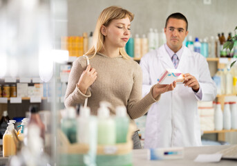 Girl choose painkiller pills box in pharmacy, examine packaging. Health care, healthy lifestyle, prevention. Parapharmaceutical products. Man pharmacist in background offers similar product