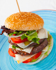 Big juicy double hamburger with cheese, fresh tomatoes, onion and lettuce leaves..