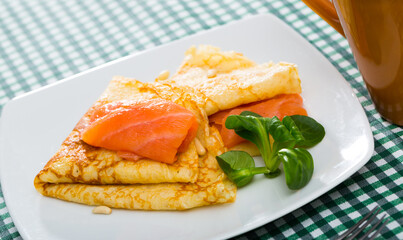 Tasty pancakes with slice of smoked salmon and spinach served on white plate