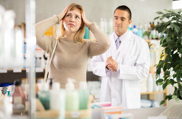 Obraz premium Woman came to a European pharmacy with a headache in search of medicine. Buyer looking for migraine pills against the background of a pharmacist