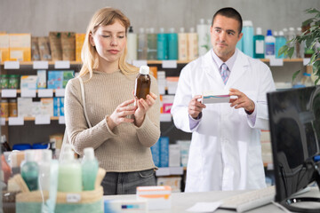 Attentive young woman choosing syrup while male pharmacist giving offer in drugstore