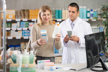 Obraz premium Careful young woman holding cream and man apothecary consulting her in drugstore