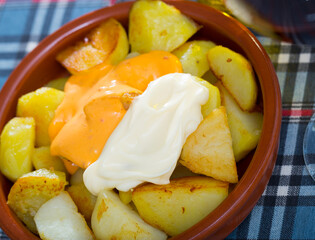 Traditional Spanish fried potatoes Patatas bravas served with cheese sauce and spicy sauce with paprika and chili in clay bowl..