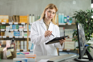 Young woman pharmacist works on a tablet, she uses a stylus to enter the number of remaining pills...