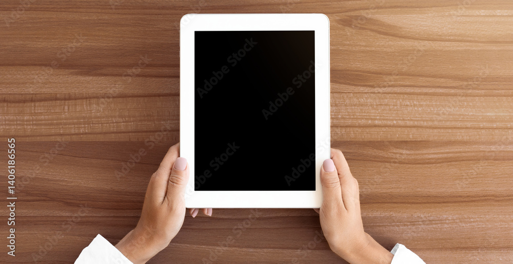 Poster Mock up image of two hands holding digital tablet with isolated black screen, wooden table in the background