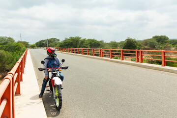A man is riding a motorcycle on a road with a bridge in the background