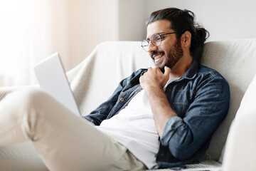 Smiling Eastern Guy With Digital Tablet Relaxing On Couch At Home, Browsing Internet, Checking New App Or Making Online Shopping, Arab Male Enjoying Modern Technologies And Domestic Leisure, Closeup