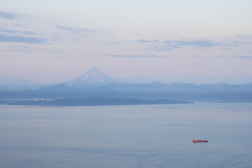 Beautiful morning landscape. View of the cargo ship in the bay. Mountains and Vilyuchinsky volcano in the distance. Avacha Bay, Pacific Ocean. Kamchatka Territory, Far East of Russia.