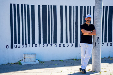 45 year old stylish white European man dressed in black and white next to wall with large barcode.