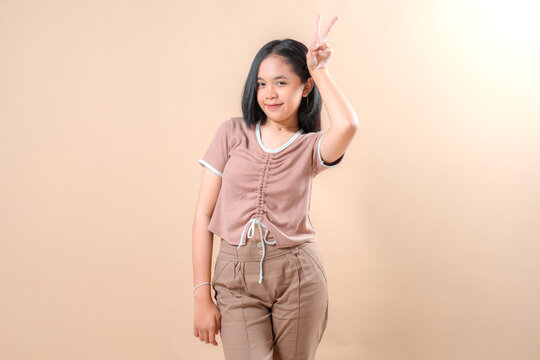 Charming young girl with a playful, flirty expression showing peace sign. Her tilted head and half-smile with tongue out convey confidence, fun, and youthful energy.