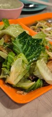 Stir-fried morning glory and crispy pork on an orange plate