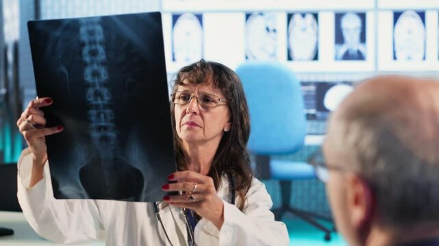 Female general practitioner giving bad worrying news to elderly man, reading the x ray results and finding a dangerous diagnosis. Scan interpretation for a concerned senior patient. Camera B.