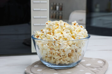 Tasty popcorn in bowl near microwave oven on white marble table indoors