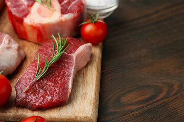 Pieces of raw beef, rosemary and tomatoes on wooden table, closeup. Space for text