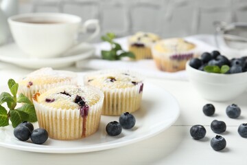 Delicious muffins with blueberries, powdered sugar and mint on white wooden table, closeup
