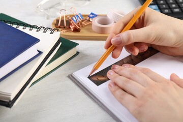 Woman drawing sketch with ruler and pencil on notebook at light table, closeup