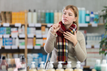 Young woman buyer with sore throat choosing medicines and hygiene products in pharmacy