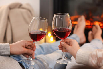 Couple with glasses of wine near fireplace on floor at home, selective focus