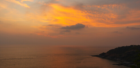 Obraz premium Golden sunset over the sea with dramatic clouds and a peaceful coastal horizon.