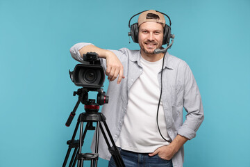 Man with professional video camera and headset on light blue background