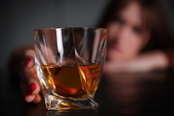 Alcohol addiction. Woman with glass of whiskey at wooden table indoors, selective focus