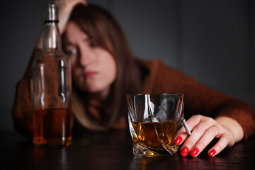 Alcohol addiction. Woman with glass of whiskey, cigarette and bottle at table indoors, selective focus