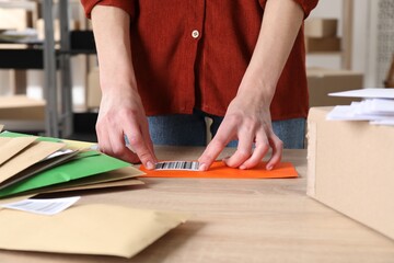 Woman putting barcode onto envelope at table in post office, closeup