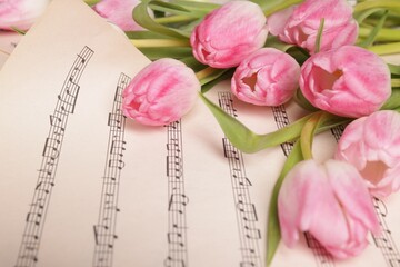 Beautiful tulips on sheet with music notes, closeup