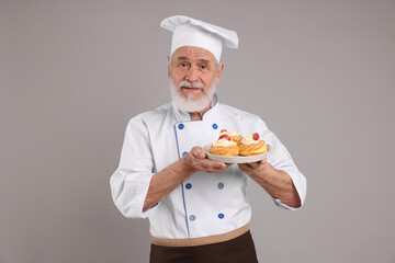 Professional pastry chef with delicious profiteroles on grey background