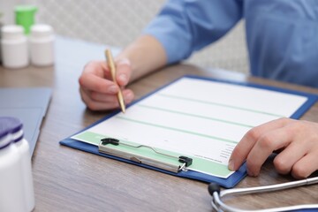 Doctor filling out patient's medical card at wooden table, closeup
