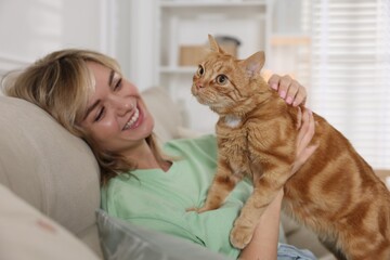 Woman with her cute ginger cat on sofa at home
