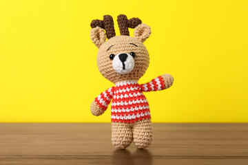 Cute knitted toy deer on wooden table against yellow background
