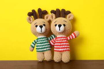 Fototapeta premium Cute knitted toy deers on wooden table against yellow background