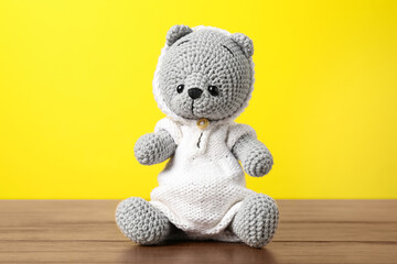 Cute knitted toy bear on wooden table against yellow background