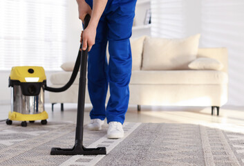 Cleaning service worker vacuuming rug with professional vacuum cleaner at home, closeup