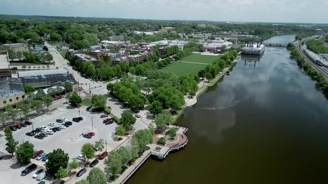 The aerial view of a Elgin town divided by Fox river, with bridges. The town with lush greenery, a mix of residential, commercial, and industrial buildings. 