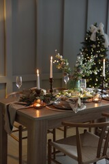 Christmas table setting with stylish dishware, glasses and burning candles in festive decorated room